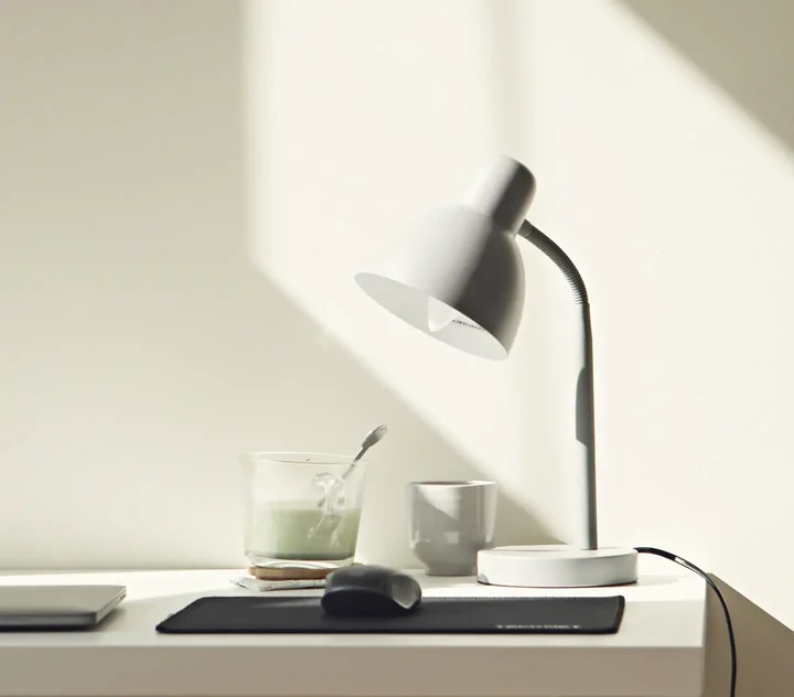 A desk with a lamp and a cup in morning sunlight.