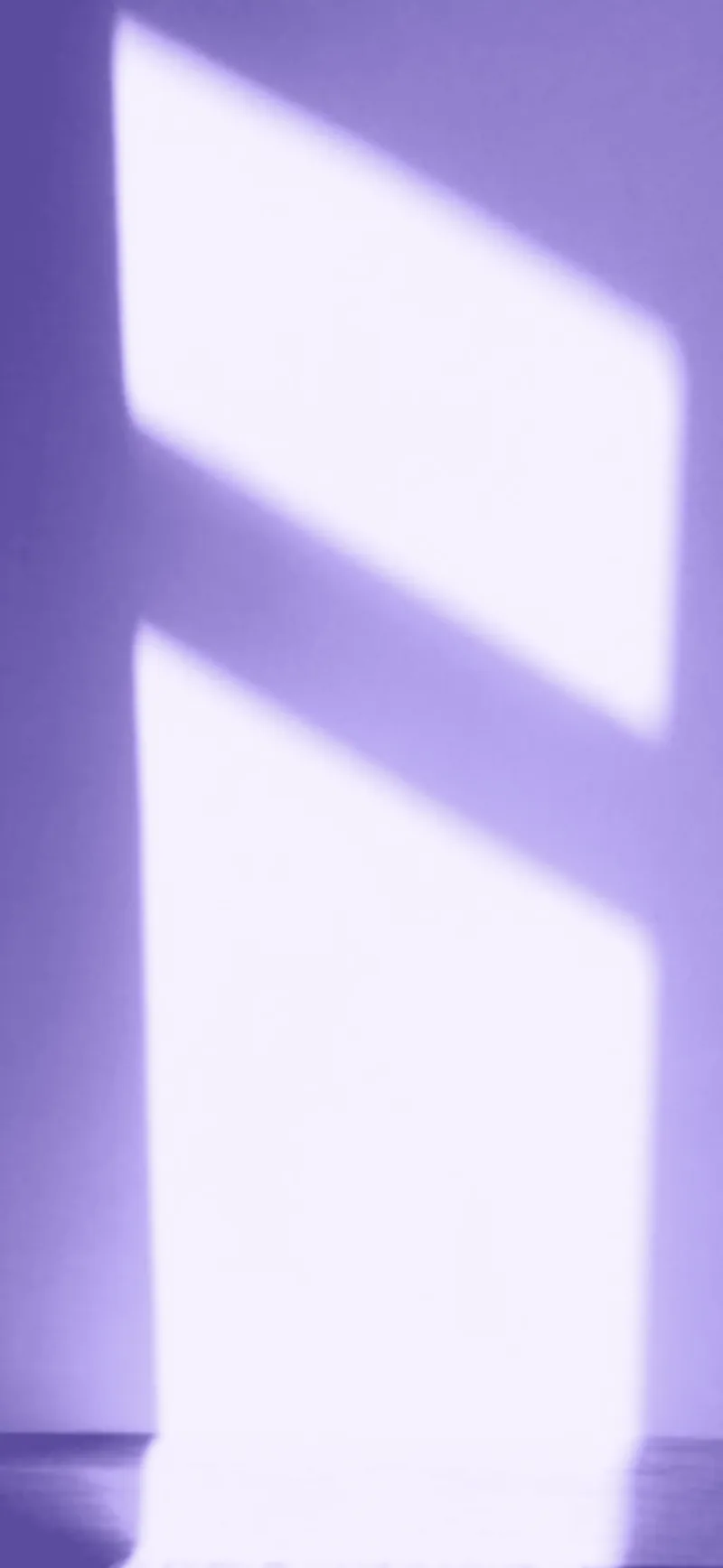 Window light falling on a plain wall, in soft lavender tones.